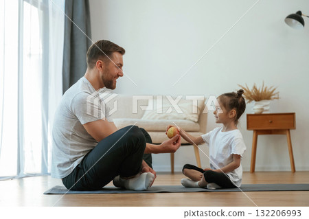 Giving an apple. Father with little daughter are doing yoga at home 132206993