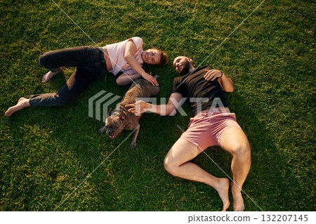 Top view, lying on the grass. Man and woman are with dog on the field 132207145