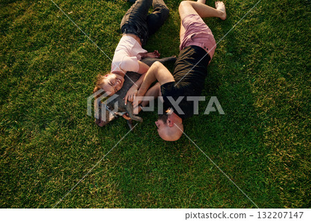 Top view, lying on the grass. Man and woman are with dog on the field Top view, lying on the grass. Man and woman are with dog on the field 132207147