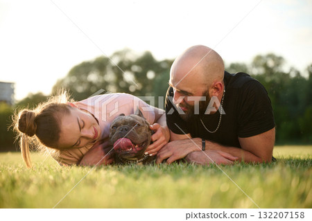 Front view, taking care of animal. Man and woman are with dog on the field Front view, taking care of animal. Man and woman are with dog on the field 132207158