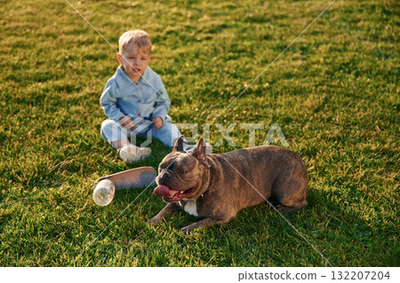 Sitting on the ground. Cute little boy is with dog on the field Sitting on the ground. Cute little boy is with dog on the field 132207204