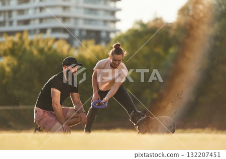 Playing with a rubber toy. Man and woman are with dog on the field Playing with a rubber toy. Man and woman are with dog on the field 132207451