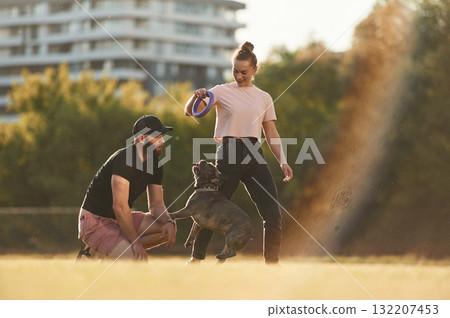Playing with a rubber toy. Man and woman are with dog on the field 132207453