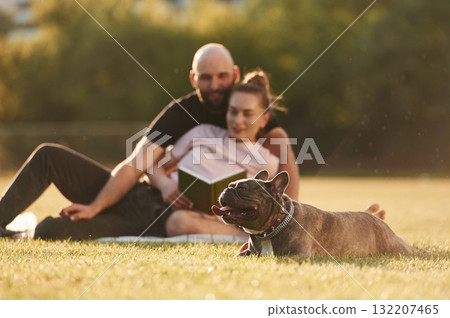 Weekend time, resting and sitting. Man and woman are with dog on the field Weekend time, resting and sitting. Man and woman are with dog on the field 132207465