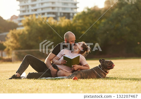 Weekend time, resting and sitting. Man and woman are with dog on the field Weekend time, resting and sitting. Man and woman are with dog on the field 132207467