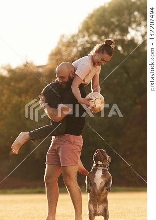 Girlfriend is with soccer ball. Man and woman are with dog on the field 132207494