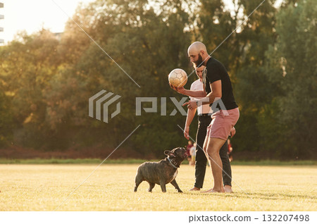 Using soccer ball, playing. Man and woman are with dog on the field 132207498