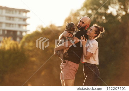 Lovely couple, holding animal in hands. Man and woman are with dog on the field 132207501
