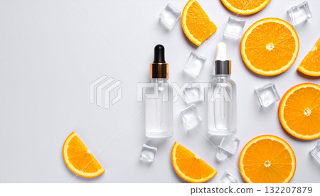A flat lay of two cosmetic serum bottles with orange slices and ice cubes on a white background with copy space. 132207879