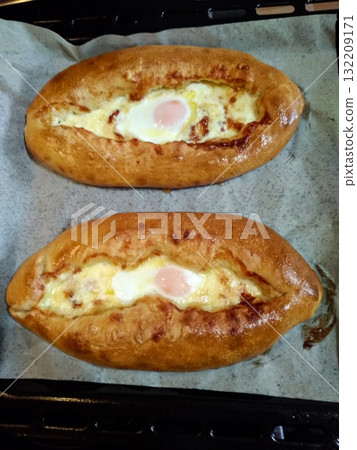 Two adjarian khachapuri baking in the oven with egg and cheese Two adjarian khachapuri baking in the oven with egg and cheese 132209171