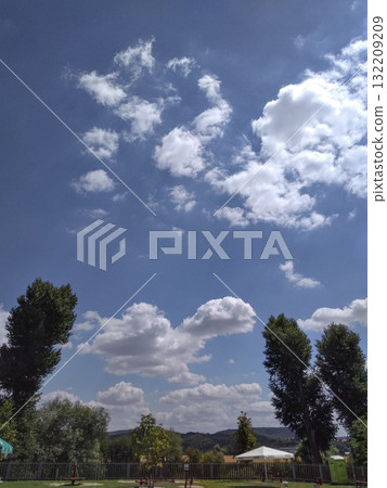 White cumulus clouds drifting across vibrant blue sky over green park 132209209