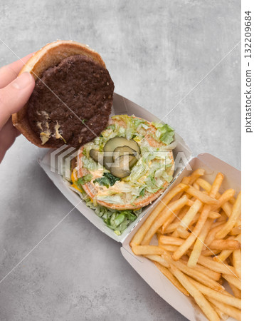 Hand holding burger patty above open big mac container with french fries galentines day 132209684