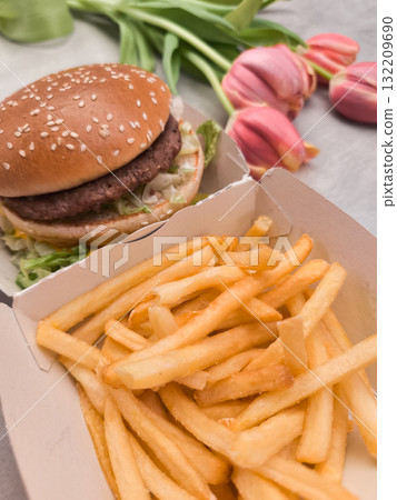 Cheeseburger and french fries with pink tulips bouquet on table galentines day Cheeseburger and french fries with pink tulips bouquet on table galentines day 132209690