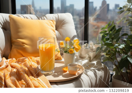 glass of orange juice and sliced oranges on table in the room, modern interior with sofa and pillows, beautiful view outside window of modern metropolis with skyscrapers 132209819