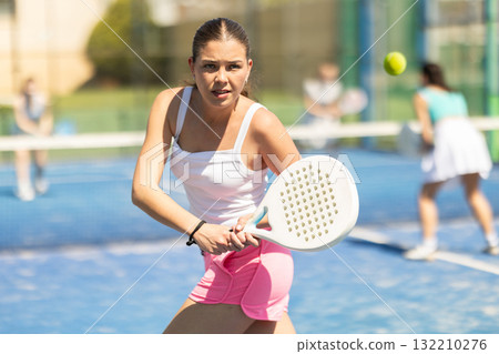 Young woman playing paddle tennis against team of women 132210276
