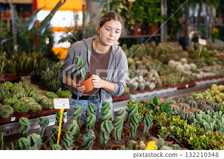 Girl works as auxiliary worker in plant store warehouse, review cactus seedling Girl works as auxiliary worker in plant store warehouse, review cactus seedling 132210348
