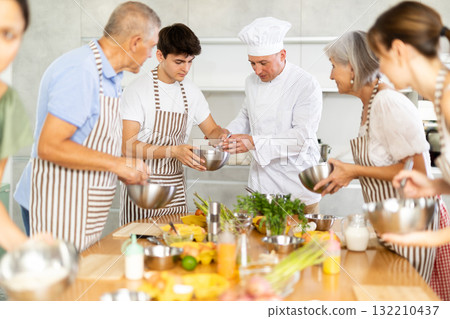 Cheerful middle-aged man chef of cooking course teaching attendees how to mix sauce 132210437