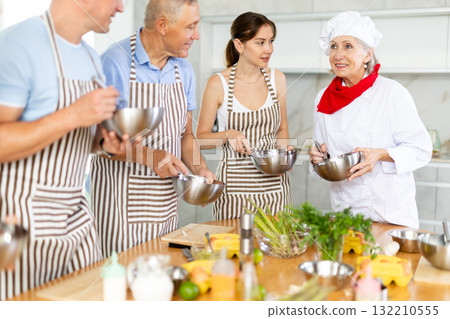 Smiling old woman chef of cooking course teaching attendees how to mix sauce 132210555