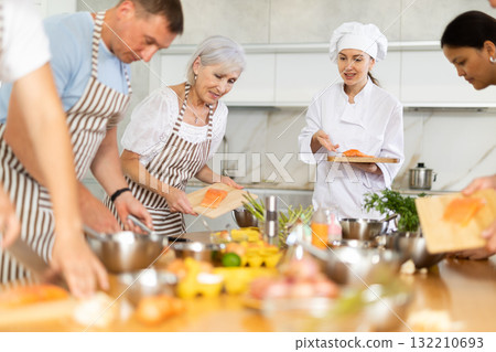 Young female cook teaches to cook group of people Young female cook teaches to cook group of people 132210693