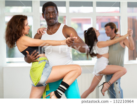 Smiling multiracial men and women enjoying partner dance while training together in studio Smiling multiracial men and women enjoying partner dance while training together in studio 132210964