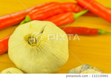 Garlic cloves and red chili peppers on a wooden cutting board. The concept of cooking and vegetables in the home. Garlic - Allium sativum is a species of bulbous flowering plants in the genus Allium Garlic cloves and red chili peppers on a wooden cutting board. The concept of cooking and vegetables in the home. Garlic - Allium sativum is a species of bulbous flowering plants in the genus Allium 132210991