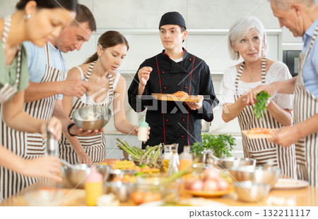 Chef in uniform teaches cooking class students how to clean and cut salmon fillet 132211117