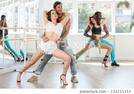 Adult couples rehearse dynamic couple dances during a group lesson in dance studio Adult couples rehearse dynamic couple dances during a group lesson in dance studio 132211153