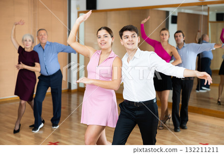 Cheerful young guy and girl practicing ballroom dances in ballroom 132211211