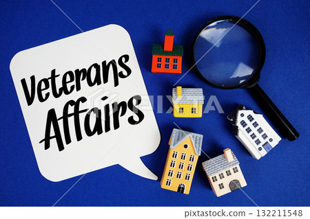 VA Veterans Affairs text with house models and magnifying glass on blue background VA Veterans Affairs text with house models and magnifying glass on blue background 132211548