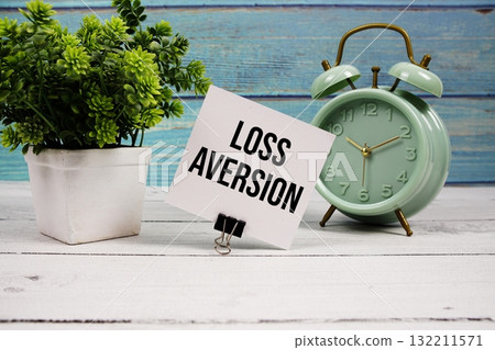 Loss Aversion text written on paper card with alarm clock on wooden background Loss Aversion text written on paper card with alarm clock on wooden background 132211571
