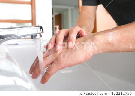 Hands of woman wash their hands in a sink with foam to wash the skin and water flows through the hands. Concept of health, cleaning and preventing germs and coronavirus from contacting hands 132211756