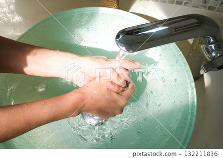 Hands of woman wash their hands in a sink with foam to wash the skin and water flows through the hands. Concept of health, cleaning and preventing germs and coronavirus from contacting hands Hands of woman wash their hands in a sink with foam to wash the skin and water flows through the hands. Concept of health, cleaning and preventing germs and coronavirus from contacting hands 132211836