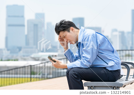 A man in work clothes looking at his smartphone and worrying A man in work clothes looking at his smartphone and worrying 132214901