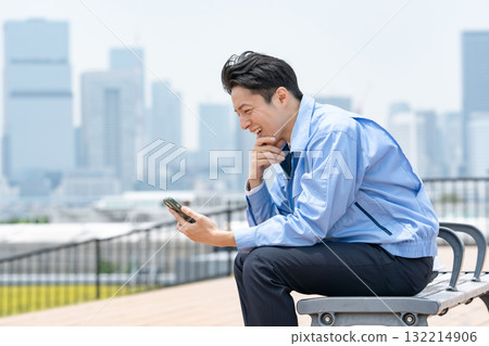 穿著工作服的男人，拿著智慧型手機，笑著 132214906