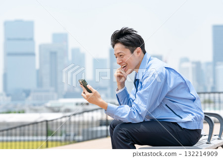 穿著工作服的男人，拿著智慧型手機，笑著 132214909