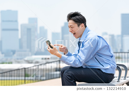 穿著工作服的男人，拿著智慧型手機，笑著 132214910