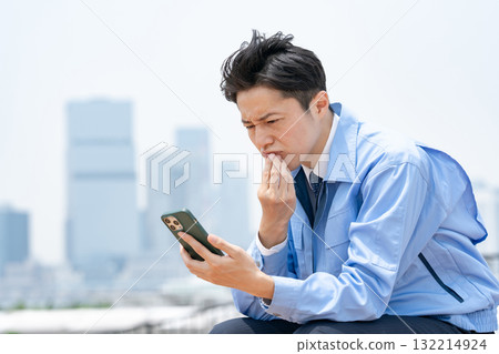 A man in work clothes looking at his smartphone and worrying 132214924