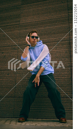 Man dancing in blue hoodie and headphones near textured brown wall Man dancing in blue hoodie and headphones near textured brown wall 132215054