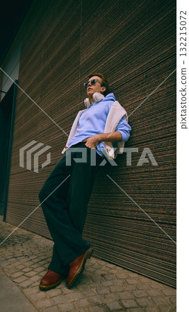 Man leaning on wall wearing light blue hoodie and white sweater outdoors Man leaning on wall wearing light blue hoodie and white sweater outdoors 132215072