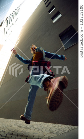 Man jumping in city alley wearing denim jacket and red checkered shirt 132215100