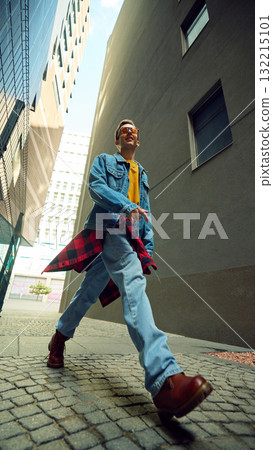 Man walking between tall buildings in denim jacket and sunglasses Man walking between tall buildings in denim jacket and sunglasses 132215101