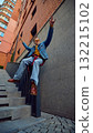 Young man sitting on stair rail in denim outfit and yellow shirt among city buildings 132215102