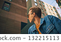 Man in denim jacket with yellow sweater looking sideways among high city buildings 132215113