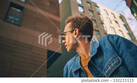 Man in denim jacket with yellow sweater looking sideways among high city buildings Man in denim jacket with yellow sweater looking sideways among high city buildings 132215113