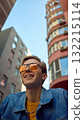 Smiling man in denim jacket with yellow shirt looking up between buildings 132215114