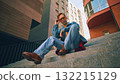 Young man sitting on stairs wearing denim outfit and orange glasses 132215129