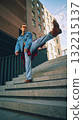 Stylish man kicking leg on city stairs in denim jacket and orange sunglasses 132215137