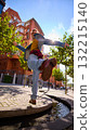 Energetic man in denim jacket kicking foot in sunlight in modern city 132215140