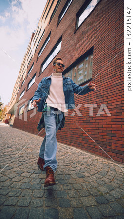 Smiling man in jeans and sunglasses walking through modern city street Smiling man in jeans and sunglasses walking through modern city street 132215147