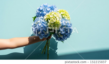 A hand holds a beautiful, elegant bouquet of fresh flowers against a bright, light blue background 132215837